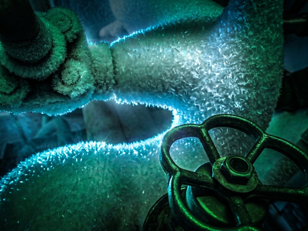 Close-up of cryogenic piping thick with frost crystals, with a cast-iron valve handwheel in the foreground